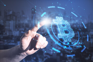 Hand pointing at abstract glowing bitcoin interface on blurry night city background. Cryptocurrency concept. Double exposure.