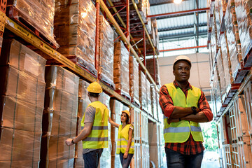 Portrait of black male worker team working in factory warehouse. Black man worker smiling with crossed arms indoor of building in background shelves with goods.Logistic industry concept.