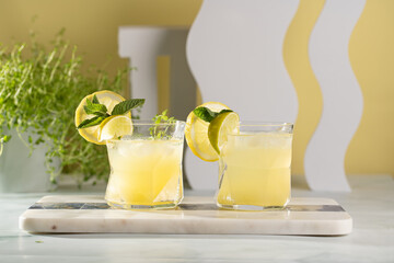 Two ice lemonade drinks in irregular glass with lime pieces and mint
