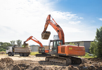 two orange crawler excavators and a gray dump truck in the process of excavation. Site preparation. Loading and transportation of soil