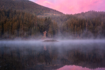 Fototapeta premium Fiery sunrise at alpine lake Synevyr, Carpathian mountains, amazing nature landscape with morning mist, forest, colored sky and reflection in the water, outdoor travel background, Zakarpattia, Ukraine