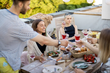 Sad and thoughtful woman sitting separately on a party with friends outdoors, young people dining on a rooftop terrace