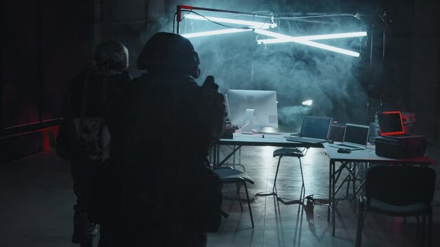 Handheld tracking shot of armed SWAT team with flashlights storming empty hackers hideout in industrial space They are checking computers for stolen data