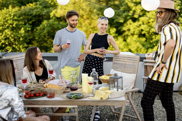 Young group of stylish people having a festive dinner on the roof terrace. Friends hanging out and...