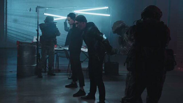 Slowmo tracking shot of special forces officer arresting hackers while other officers securing their dark hideout