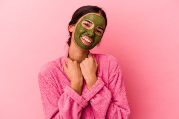 Young caucasian woman wearing a bathrobe and facial mask isolated on pink background
