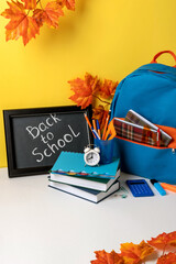 School backpack with colorful school supplies  and blackboard with letters back to school. School supplies on yellow background.