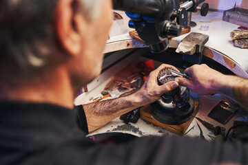 Man bringing burnisher to gem in ring during jewelry work