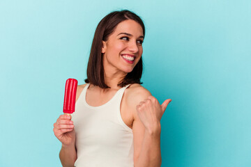 Young caucasian woman holding an ice cream isolated on blue background points with thumb finger away, laughing and carefree.