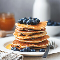 Stack of pancakes with blueberries and syrup on white plate, closeup view. Sweet breakfast food....