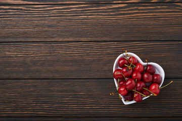 Cherry with water drops on heart shaped plate on dark brown stone table. Fresh ripe cherries. Sweet red cherries. Top view. Rustic style. Fruit Background