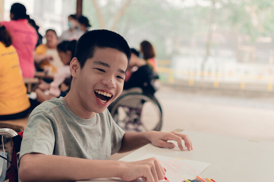 Happy Asian Disabled Teen Boy On Wheelchair Writing And Learning In Special Education School, Skill Development Concept.