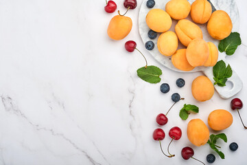 Naklejka na ściany i meble Fresh apricots, red cherry and blackberry on white marble background. Vegetarian, weight loss, clean and healthy eating concept. Top view. Copy space.