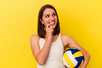 Young caucasian woman playing volleyball isolated on yellow background relaxed thinking about...