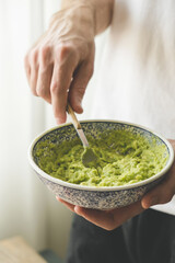 Male chef mashing avocado with fork in a bowl. Making guacamole sauce - obrazy, fototapety, plakaty