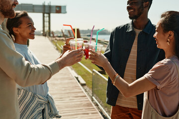 Side view portrait of young people clinking cocktail glasses in Summer while enjoying party outdoors