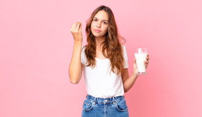 young pretty woman making capice or money gesture, telling you to pay and holding a glass of milk