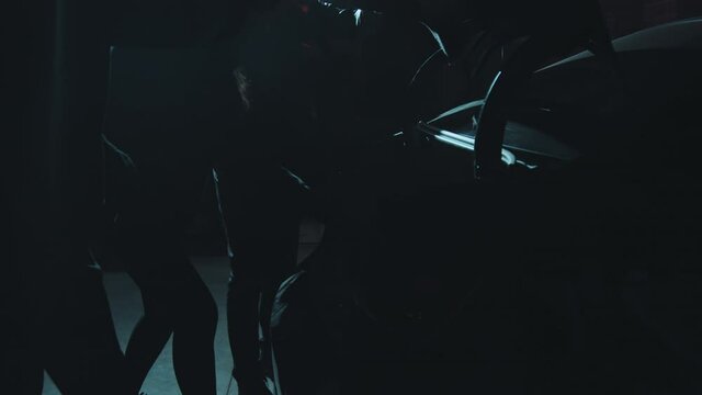 Handheld slowmo tracking shot of masked robbers opening trunk of car and checking bag full of money, then high-fiving each other