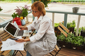 Mature businesswoman working with gadgets in terrace in village
