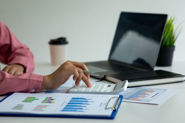 Close up of business woman hand holding a pen with calculator report computational concepts statistic graph placed at home office.analyzing report, business performance concept,