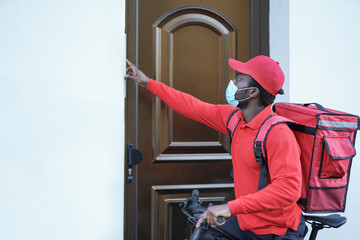 African american delivery man with bicycle ringing on doorbell while wearing safety face mask for coronavirus outbreak
