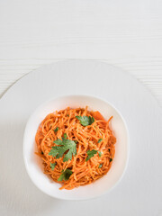 Spicy Asian salad with grated carrots and parsley. Over white background Korean carrots in a white bowl. Salad in a plate on a white stand. Vegetarian diet. Healthy food concept. View from above