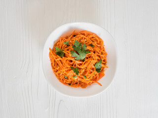 Spicy Asian salad with grated carrots and parsley. Korean carrots in a white bowl on a white backgroung. Vegetarian diet. Healthy food concept. View from above