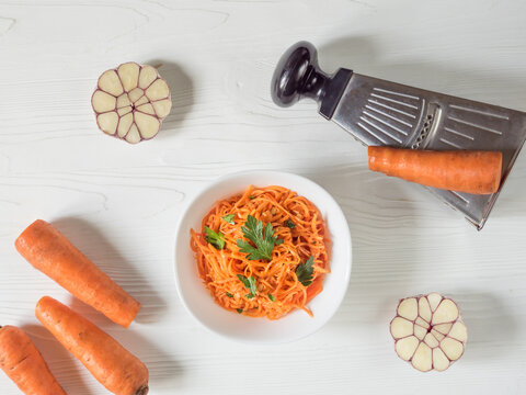 Spicy Asian Salad With Grated Carrots And Parsley. On A White Background Korean Carrots In A White Bowl With Ingredients For Making Salad. Vegetarian Diet. Healthy Food Concept. View From Above