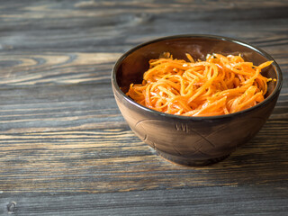 Spicy Asian salad with grated carrots. Korean carrot in a dark bowl on a brown wooden background. Vegetarian diet. Healthy food concept. Horizontally. Copy space