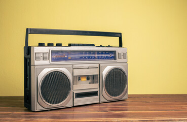 Retro portable stereo radio cassette recorder on wooden table on yellow background.