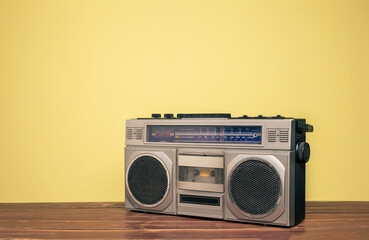 Retro portable stereo radio cassette recorder on wooden table on yellow background.
