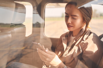 Fototapeta na wymiar Beautiful young woman using smartphone in aircraft