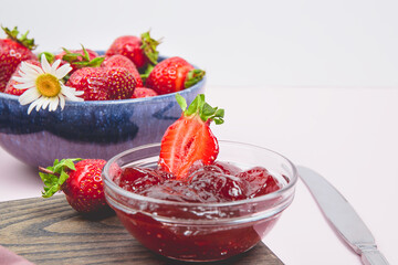 Homemade strawberry jam or strawberry jelly with fresh ripe strawberries on a white plate. Breakfast with bread toast with strawberry jam. Knife for spreading jam. Summer preserves.