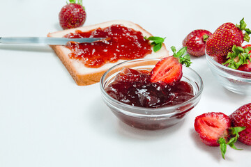 Homemade strawberry jam or strawberry jelly with fresh ripe strawberries on a white plate. Breakfast with bread toast with strawberry jam. Knife for spreading jam.