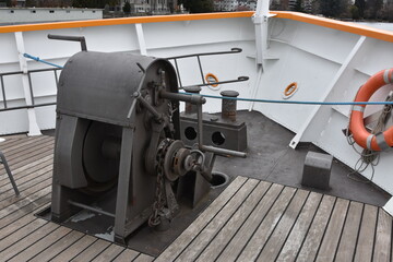 Anchor gear fixed in bow of a tourist cruiser ship painted white. On main weather bottom deck is also installed double bollards and wooden boarder floor. 