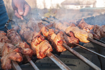 A man prepares barbecue on skewers in the grill with smoke.
