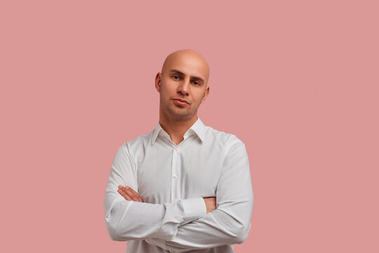 Why should I love you. Portrait of grumpy but calm bald guy with stubble, keeping his arms crossed, feeling dissatisfied after his boyfriend came home late at night. Isolated over pink background.