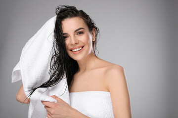 Happy young woman drying hair with towel after washing on light grey background. Space for text