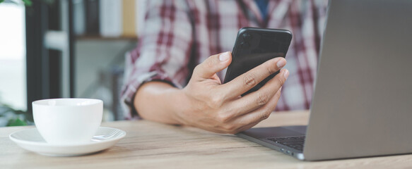 Close-up businessman holding a pen, smartphone and pointing at financial graph checking business report on wooden desk with computer laptop besided at home. Stock photo