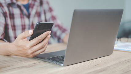 Close-up businessman holding a pen, smartphone and pointing at financial graph checking business report on wooden desk with computer laptop besided at home. Stock photo