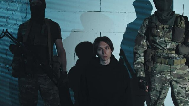 Portrait dolly-in shot of man being held hostage by armed terrorists in balaclavas