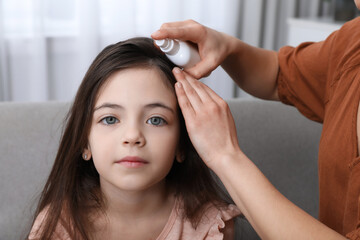 Fototapeta premium Mother using lice treatment spray on her daughter's hair indoors