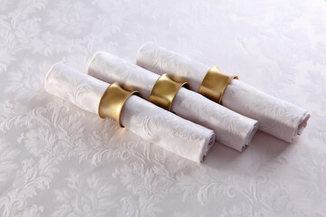 Festive table setting.Napkins made of cotton with brass rings.Napkin rings made of yellow metal.The concept of holidays.White tablecloth with a textured pattern.A copy of the space.