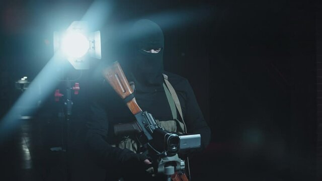 Slowmo tracking shot of unrecognizable armed terrorist with weapon filming hostage off camera