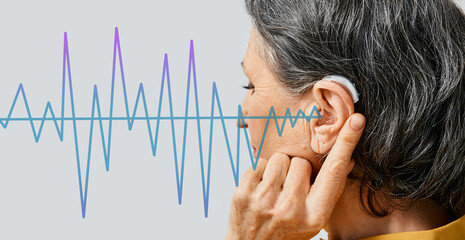 Hearing aids. Senior woman wearing behind the ear hearing aid with sound waves pattern in...