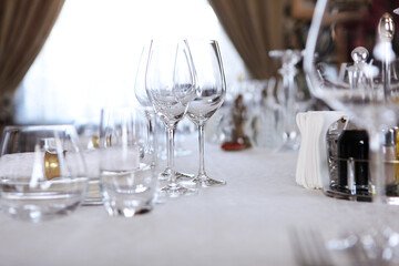 Festive table setting.Napkins made of cotton with brass rings.Concept of holidays.Wine glasses on table. White plates.VIP lounge. White tablecloth with textured pattern.Out of focus. 
