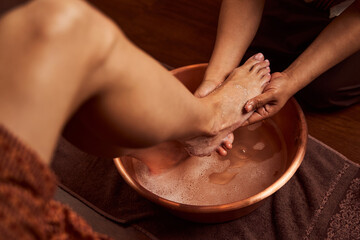 Experienced chiropodist washing foot in special container in spa salon