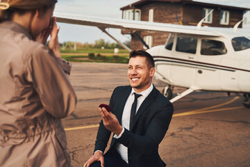 Cheerful man making proposal to his girlfriend at airdrome - Powered by Adobe