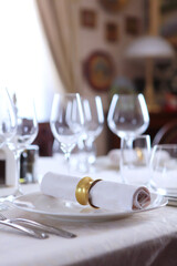 Cotton napkin with a ring made of yellow metal.The concept of holidays.Wine glasses on the table. White plates.Festive table setting. White tablecloth with a textured pattern. Out of focus. 