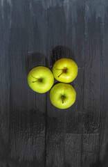 Top view of three fresh green golden apples on a rustic table